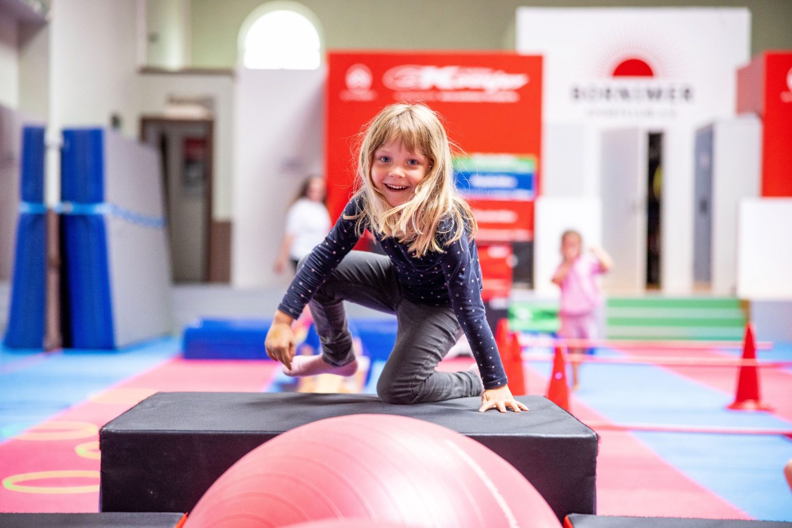 Kind klettert lachend über einen Kasten in der Sporthalle